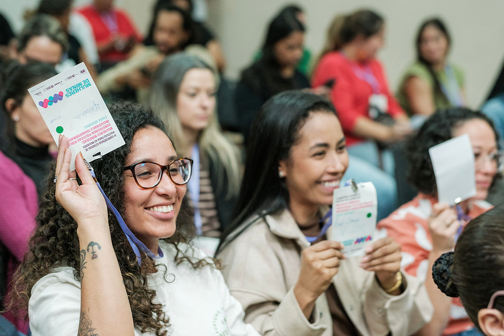 #PraTodosVerem: Mulheres de diferentes idades, sentadas em auditório, levantam cartões coloridos e sorriem durante a votação das propostas da conferência municipal.
