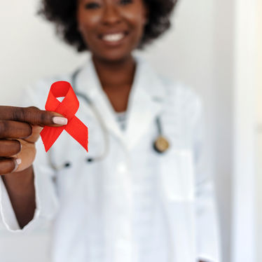 A Black woman doctor is holding a red ribbon in a display of support, and to raise awareness for World AIDS Day.