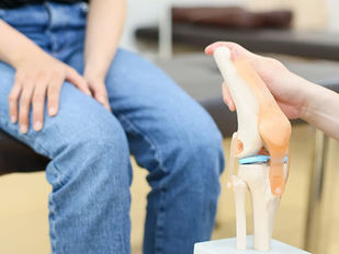 膝を抑える少年と模型で膝の仕組みを説明する医師の手元