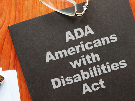 Black notebook with "ADA Americans with Disabilities Act" text on a wood background, next to a gold-trimmed pen and glasses.