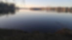 A landscape photo of a calm lake with some trees in the background.