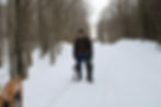 Brent Bowyer holding snowshoes in the middle of a snowy landscape, with trees on the left and right.
