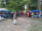 Tents selling goods under some trees. A person stands in the foreground.