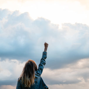 View from behind of a young woman lifting her arm high up in a triumphant gesture