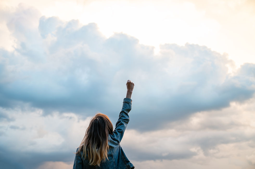 View from behind of a young woman lifting her arm high up in a triumphant gesture