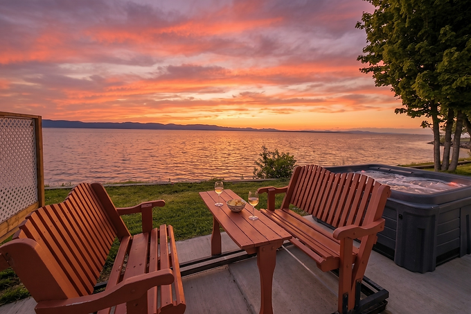 Terrasse du chalet 8 avec chaises en bois et spa au coucher du soleil sur le fleuve