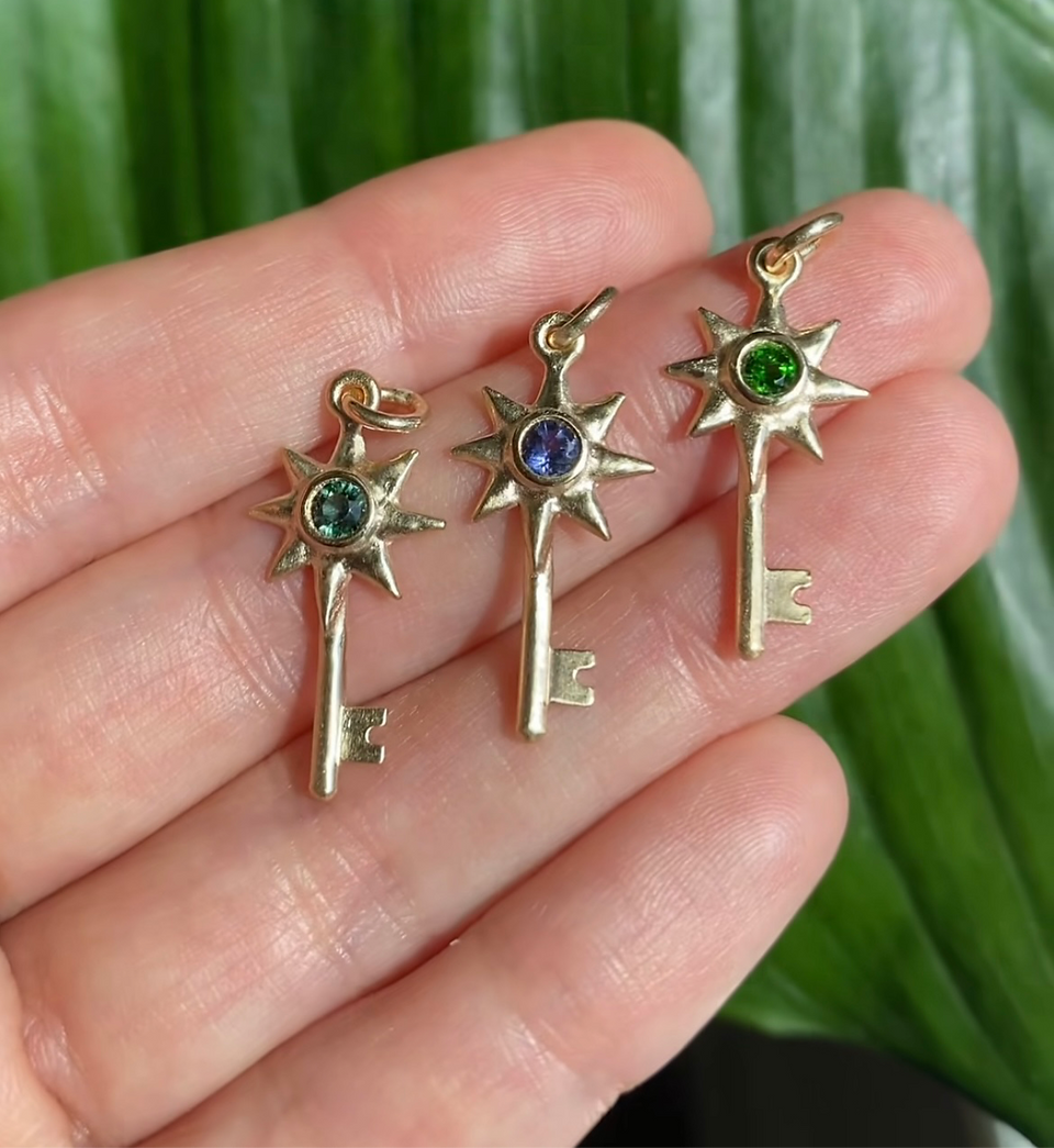a hand holding three sun keeper charms in yellow gold and gemstones