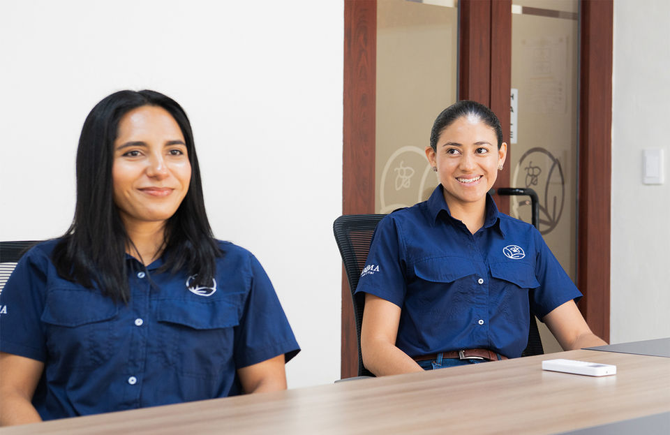 Dos empleados de ACM se sientan en una mesa en una sala de reuniones, sonriendo y vistiendo uniformes azul marino de la empresa.