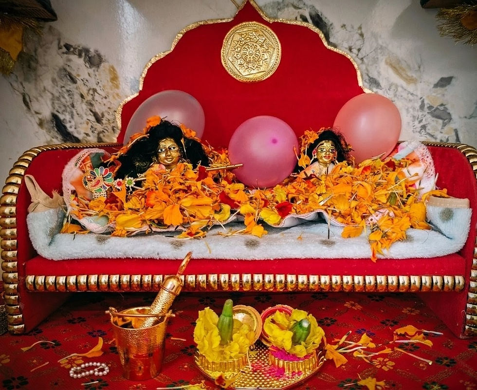 Eye-level view of a small altar with Krishna and Radha idols decorated with colorful flowers and gulal powder