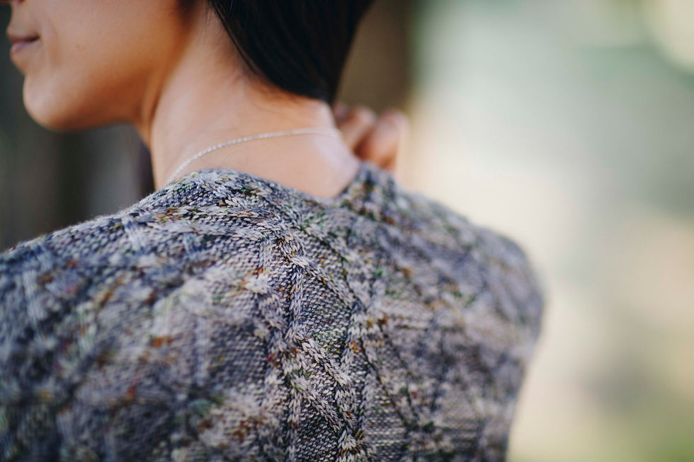 Thumbnail: Back neck cropped view of a woman wearing cabled cardigan. Color is gray with speckles.
