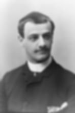Black and white portrait of a man with short hair and a mustache, wearing a dark suit and white collar. Neutral expression, plain background.