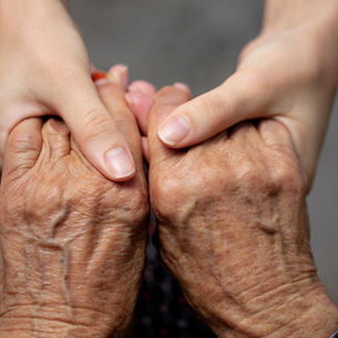 Younger hands gently holding an elderly parent's hands, reflecting caregiver support and undue influence risk in Florida