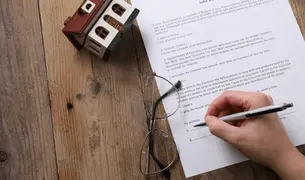 Hand signing a Florida will with reading glasses and a model house on a wooden desk, estate planning