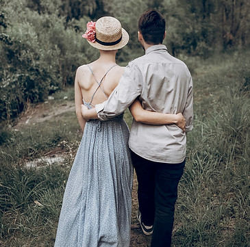 A young couple dressed as cool hipsters walk with their arms around each other away from the camera during an engagement photo shoot at a forest in Cardiff, South Wales