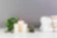 Spa decor featuring illuminated candles, stack of towels, spa stones, and green plant atop white tabletop