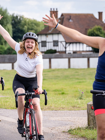 3 smiling female cyclists waving to camera