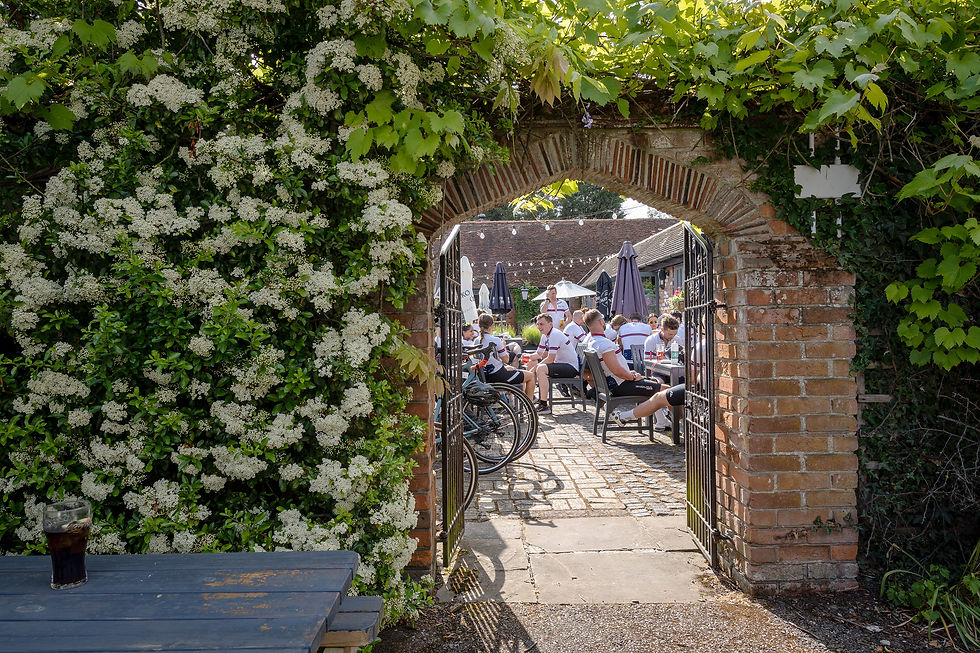 A group of cyclists in a pub garden visible through an arch in a flower covered wall