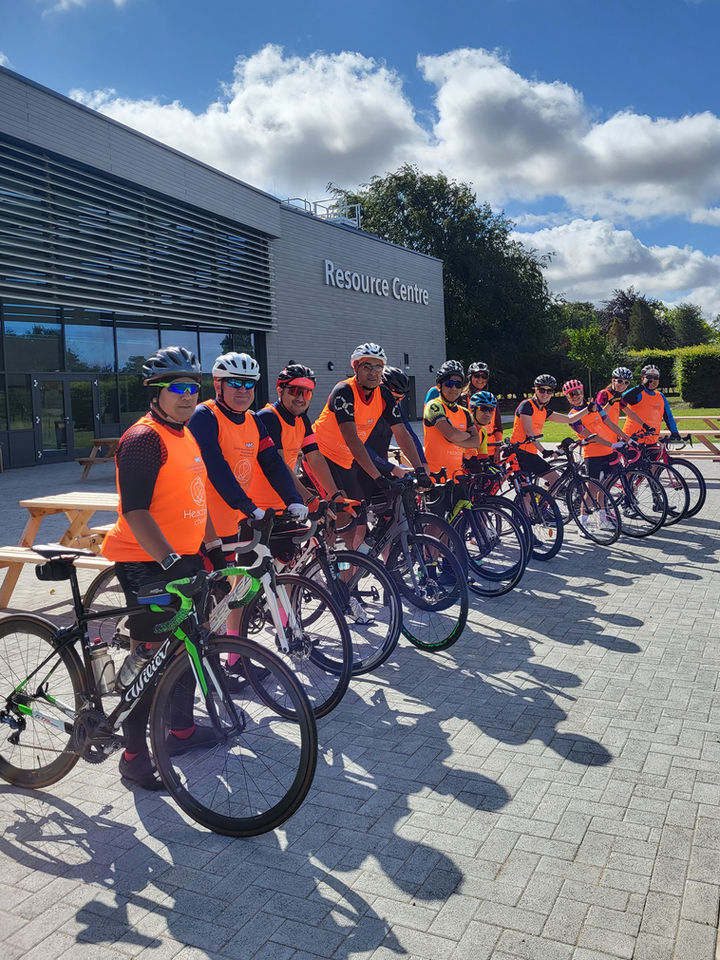 Cyclists in a line with their bikes wearing orange vests