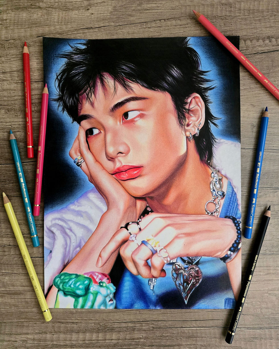 Portrait de Hyunjin terminé aux crayons de couleur, posé sur une table en bois et entouré de crayons, avec fond noir et halo bleu mettant le dessin en valeur.