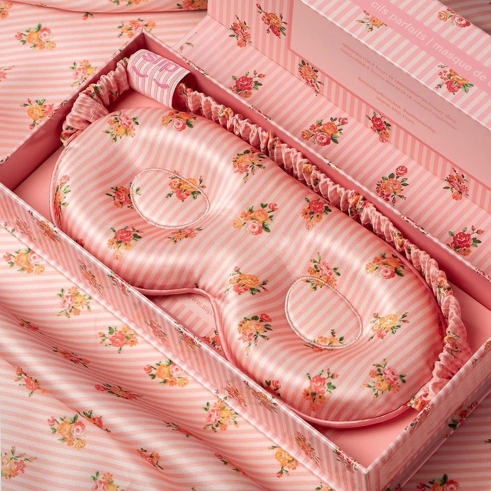 Pink floral striped sleep mask in box, surrounded by matching fabric and packaging. Elegant, feminine design conveys a soothing mood.