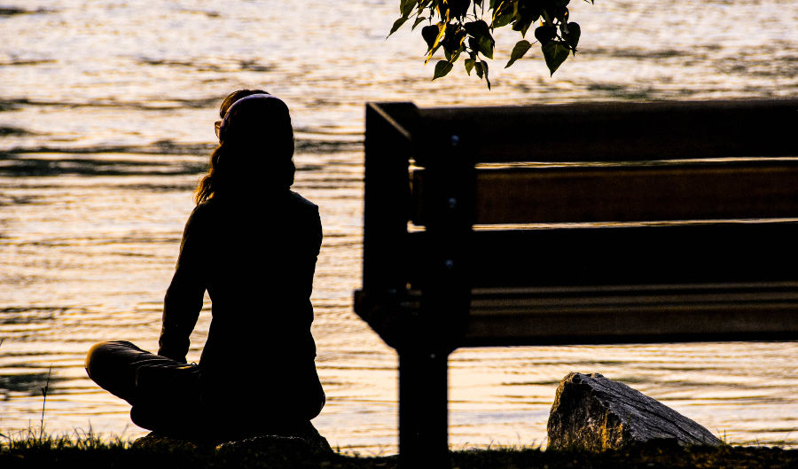 woman in silhouette by the bench and water reflecting
