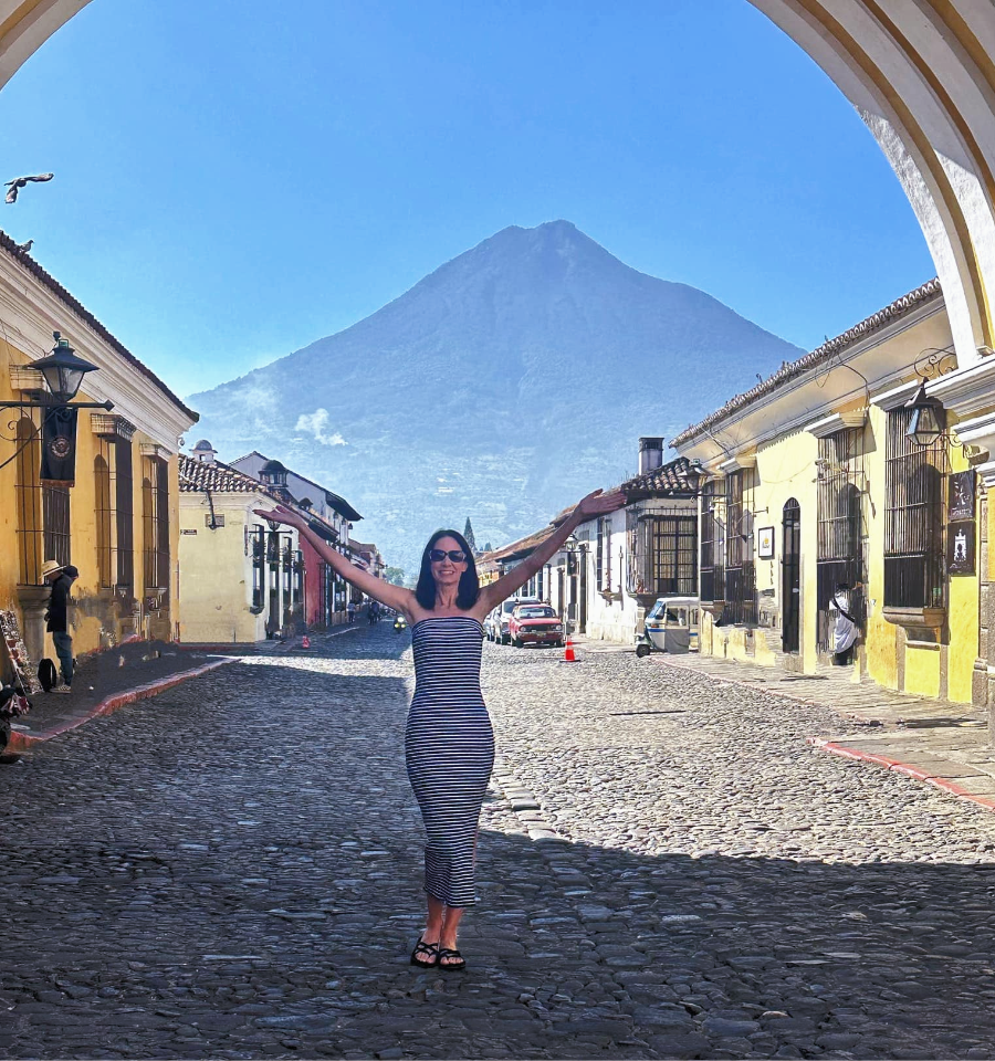 female traveler smiling under Santa Catalina Arch with Volcano Agua at the backdrop in Antigua Guatemala
