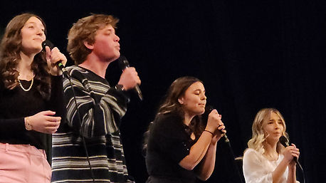 A group of 4 highschool kids, 1 boy and 3 girls, singing at a Prodigy Music Academy Concert