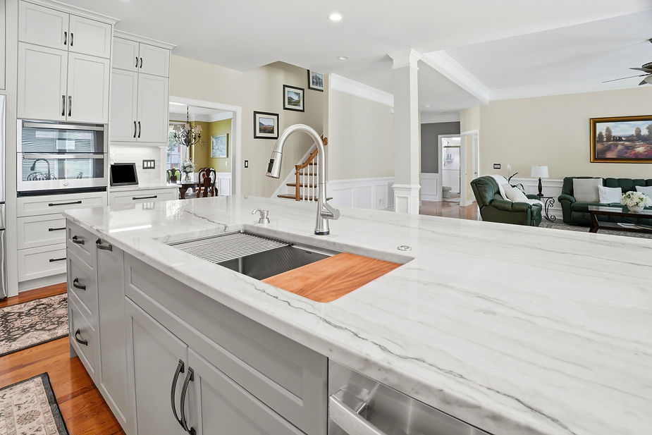 Spacious kitchen island with integrated sink, quartz countertops, white shaker cabinets, and open views into the living room and staircase.