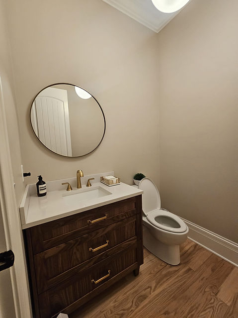 Modern powder room featuring a custom walnut vanity, white quartz countertop, brass faucet, round mirror, and warm neutral finishes with luxury design details.
