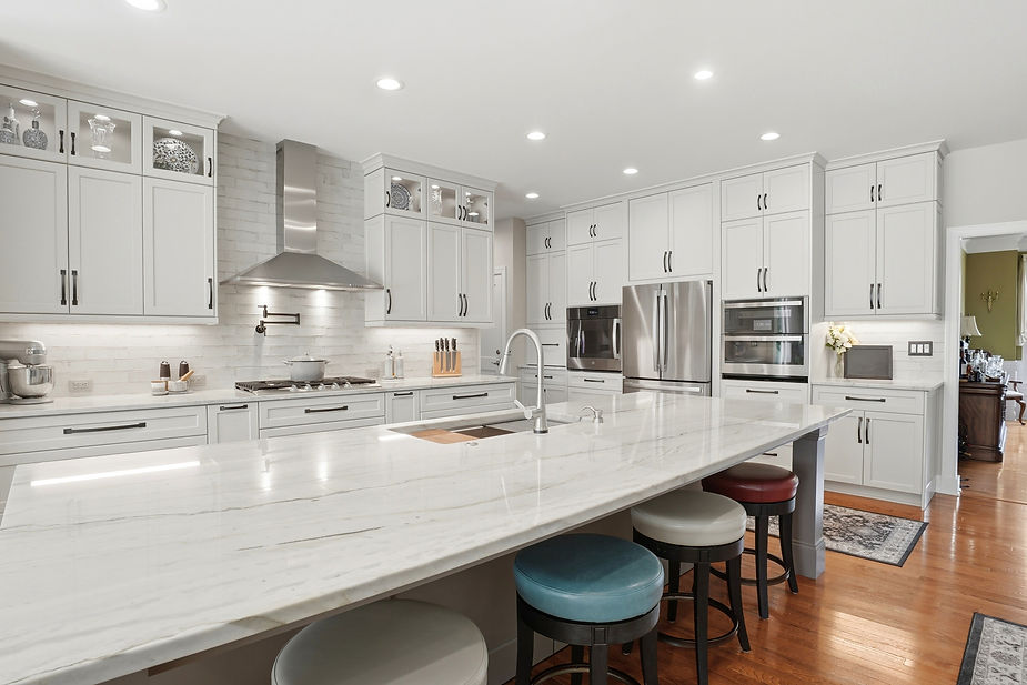 Modern custom kitchen with expansive quartz island, white shaker cabinetry, stainless steel appliances, and colorful island seating in an open floor plan.