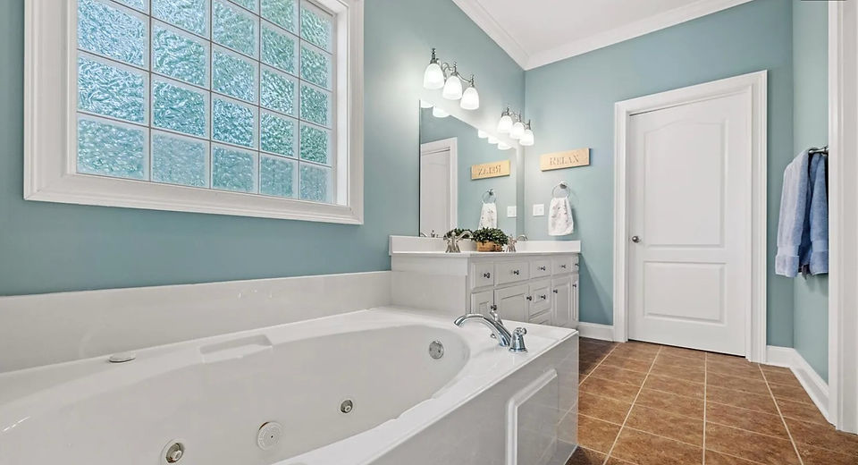Existing bathroom with a large soaking tub, double vanity, glass-block window, and traditional finishes prior to remodeling.