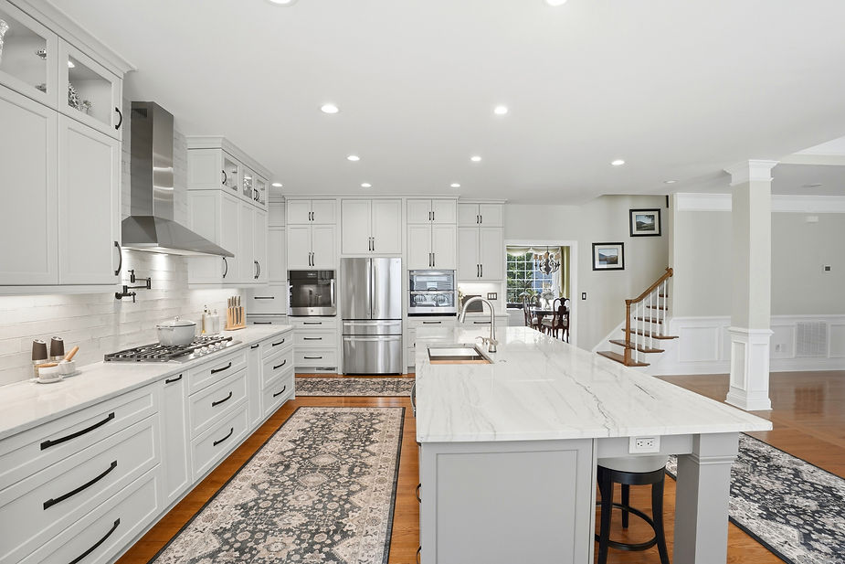Luxury kitchen featuring white shaker cabinets, oversized quartz island, stainless steel appliances, custom storage, and an open layout with classic architectural details.