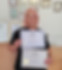 A woman with pink hair, smiling and holding two professional grooming certificates, standing in an office