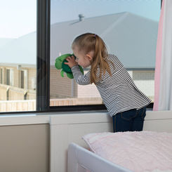 Child leaning against window fitted with Prowler Proof Guardian fall prevention window screen.