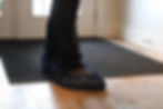 A work boot covered in a protective bootie stepping from a doormat onto hard wood floors