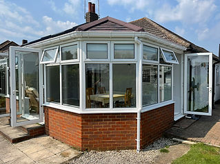 A sunlit conservatory with large glass windows and a pitched roof 