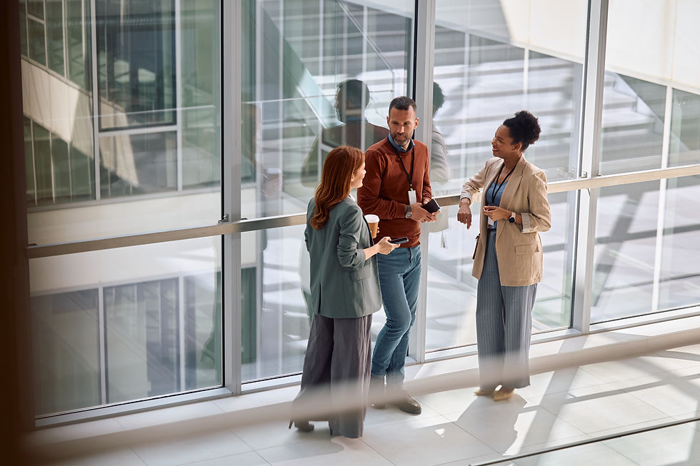 Three coworkers stand in a light-filled hallway chatting.