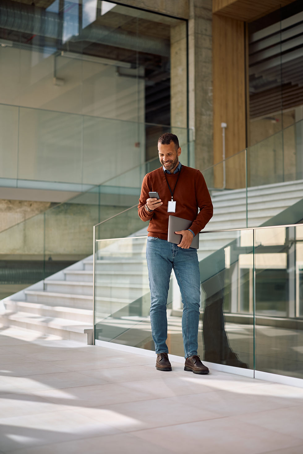 Man smiles and texts on his cell phone in an office hallway.