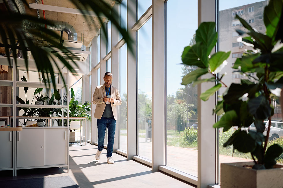 Man smiles as he walks down an office hallway texting on his phone.
