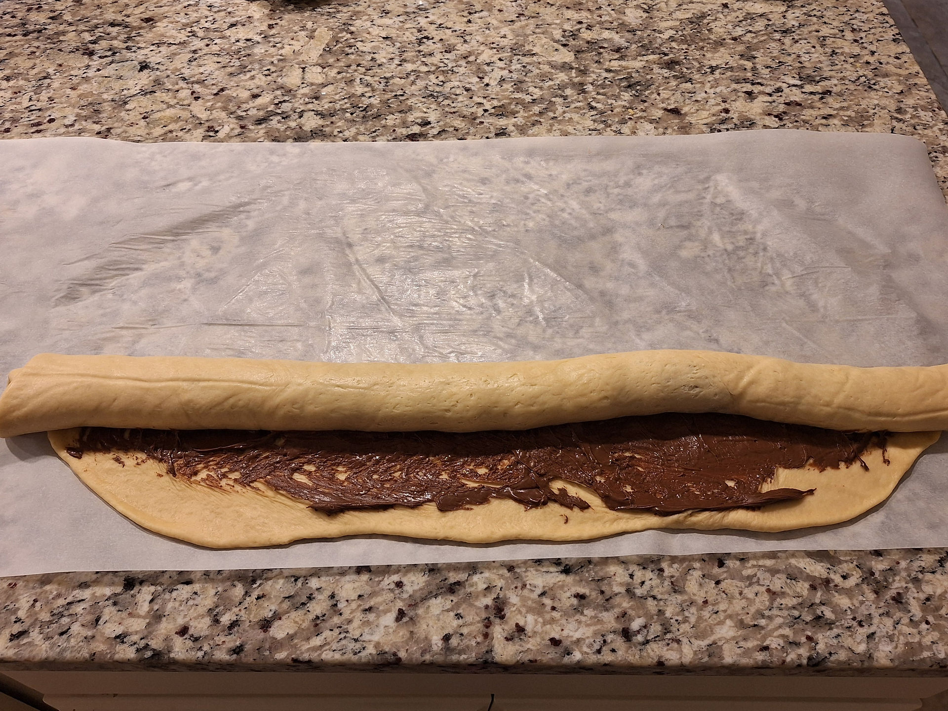 Punch down the risen dough and roll it out on a floured surface into a large rectangle. Spread an even layer of Nutella over the dough. Roll the dough tightly from one edge into a log. Slice the log in half lengthwise, exposing the layers of Nutella. Twist the two halves together to form a braid. Place the twisted dough into a greased loaf pan.