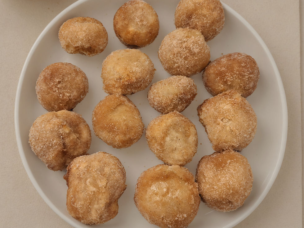A white plate with sugar-coated doughnut holes on a beige table, each golden-brown and textured, creating a cozy, appetizing scene.