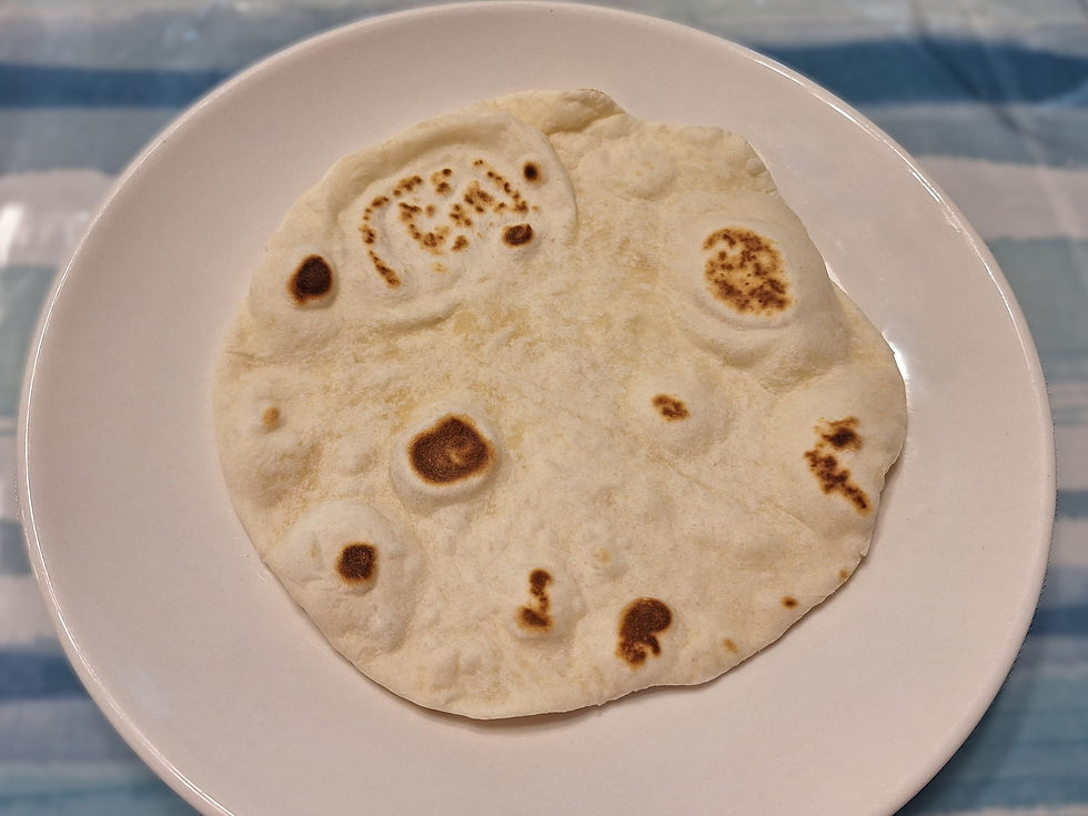 Tortilla with brown spots on a white plate, set on a blue-striped tablecloth. Warm, simple setting.