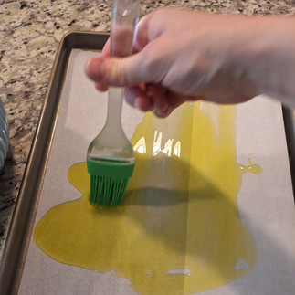 hand brushing oil on a parchment covered cooking sheet