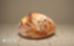 A rustic loaf of bread with a golden crust sits on a wooden surface, surrounded by crumbs. Text reads aikitchen.blog.