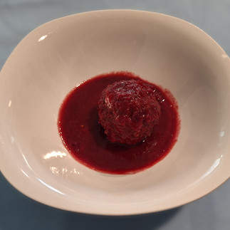 A single kibbeh with some beetroot sauce in a white bowl