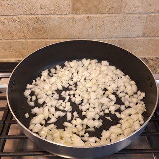frying pan with olive oil on cooktop with raw onion