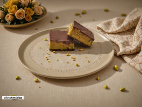 Chocolate-covered pistachio bars on a beige plate, surrounded by scattered nuts. Yellow roses and a patterned cloth in the background.