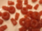 Red gummy candies shaped like bears and rings on a white surface. The gummies have a glossy texture and are scattered randomly.