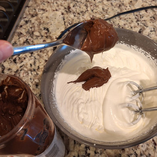 heavy whipping cream in bowl whipped and nutella being added using spoon