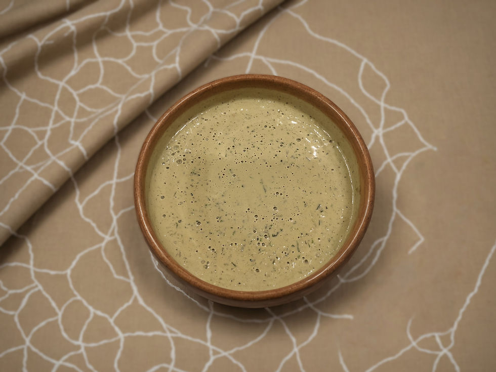 A brown bowl of creamy green sauceon a beige, patterned cloth. The soup has a speckled texture, creating a cozy and inviting mood.